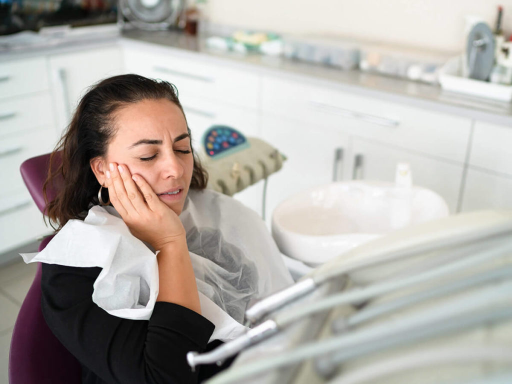 woman at a dentist office, holding her cheek in pain