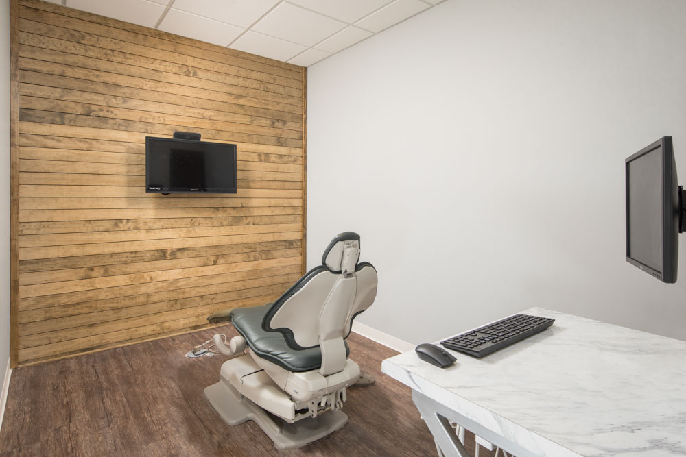 A dental exam room with an exam chair in the middle facing a tv on the wall