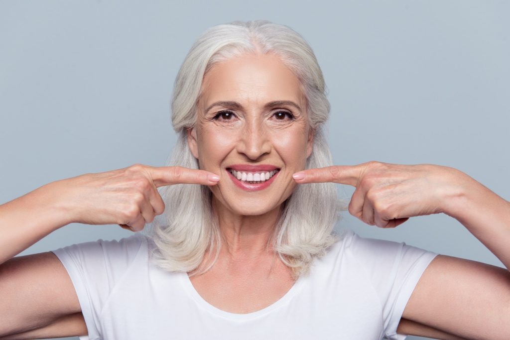 An older woman pointing to her white smile with both hands