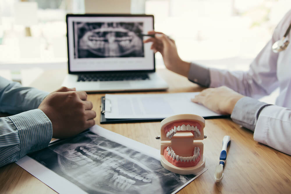 A dentist sits across a desk from a dental patient and discusses their smile design plan