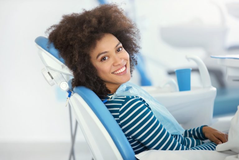 A female dental patient sits in an exam chair while looking over her shoulder and smiling
