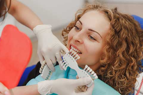 dentist compares which shade of tooth color matches the patient's teeth